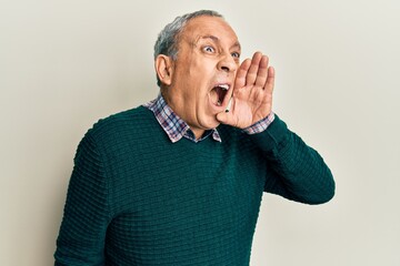 Poster - Handsome senior man with grey hair wearing casual sweater shouting and screaming loud to side with hand on mouth. communication concept.