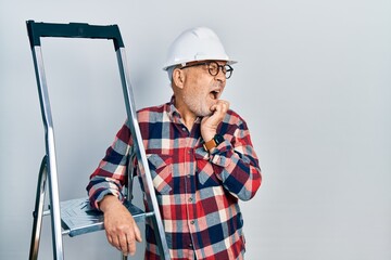 Canvas Print - Handsome mature handyman close to construction stairs wearing hardhat looking stressed and nervous with hands on mouth biting nails. anxiety problem.