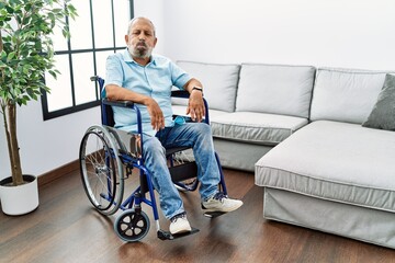 Canvas Print - Handsome senior man sitting on wheelchair at the living room puffing cheeks with funny face. mouth inflated with air, crazy expression.