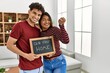 Young latin couple smiling happy holding our first home blackboard and key at house.