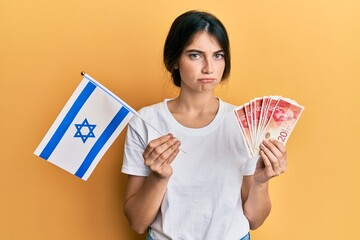 Poster - Young caucasian woman holding israel flag and shekels banknotes depressed and worry for distress, crying angry and afraid. sad expression.