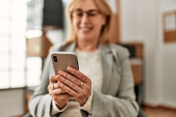 Wall Mural - Middle age businesswoman smiling happy using smartphone at the office.