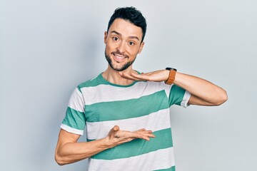 Poster - Young hispanic man wearing casual clothes gesturing with hands showing big and large size sign, measure symbol. smiling looking at the camera. measuring concept.