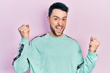 Poster - Young hispanic man wearing casual clothes screaming proud, celebrating victory and success very excited with raised arms