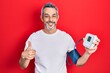 Handsome middle age man with grey hair using blood pressure monitor smiling happy and positive, thumb up doing excellent and approval sign