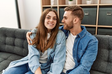 Sticker - Young caucasian couple sitting on the sofa hugging at home.