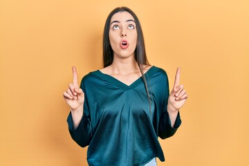 Poster - Beautiful woman with blue eyes wearing elegant shirt amazed and surprised looking up and pointing with fingers and raised arms.