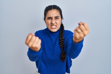 Poster - Young hispanic woman standing over isolated background angry and mad raising fists frustrated and furious while shouting with anger. rage and aggressive concept.