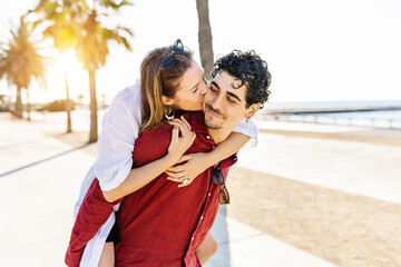 Happy couple in love enjoying their summer vacation together - Man piggybacking his girlfriend while she kissing him - Vacation and relationship concept.