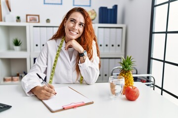 Poster - Young redhead woman nutritionist doctor at the clinic with hand on chin thinking about question, pensive expression. smiling with thoughtful face. doubt concept.