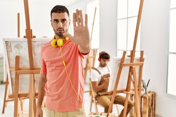 Sticker - Young hispanic man at art studio doing stop sing with palm of the hand. warning expression with negative and serious gesture on the face.