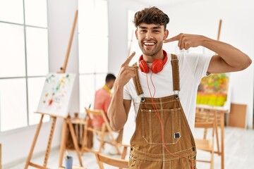 Canvas Print - Young hispanic man at art studio smiling cheerful showing and pointing with fingers teeth and mouth. dental health concept.