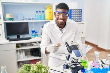 Sticker - Young african american man wearing scientist uniform using microscope at laboratory