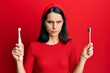 Young hispanic woman choosing electric toothbrush or normal teethbrush skeptic and nervous, frowning upset because of problem. negative person.