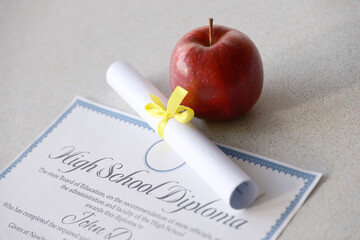 Wall Mural - A high school diploma lies on table with small scroll and red apple. Education documents