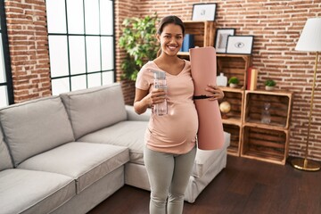 Sticker - Young pregnant woman holding yoga mat at home smiling with a happy and cool smile on face. showing teeth.