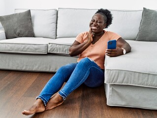 Poster - Young african woman using smartphone sitting on the floor at home touching mouth with hand with painful expression because of toothache or dental illness on teeth. dentist concept.