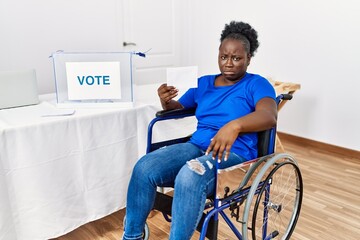 Canvas Print - Young african woman sitting on wheelchair voting putting envelop in ballot box depressed and worry for distress, crying angry and afraid. sad expression.