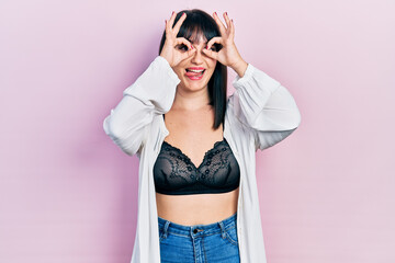 Canvas Print - Young hispanic woman wearing lingerie doing ok gesture like binoculars sticking tongue out, eyes looking through fingers. crazy expression.