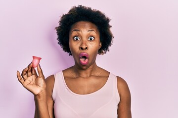 Canvas Print - Young african american woman holding menstrual cup scared and amazed with open mouth for surprise, disbelief face