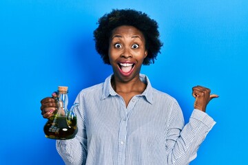 Poster - Young african american woman holding olive oil can pointing thumb up to the side smiling happy with open mouth