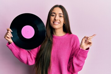 Poster - Young hispanic girl holding vinyl disc smiling happy pointing with hand and finger to the side