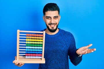 Handsome man with beard holding traditional abacus celebrating achievement with happy smile and winner expression with raised hand