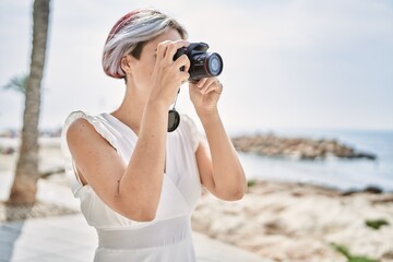 Sticker - Young caucasian girl smiling happy using professional camera at the beach.