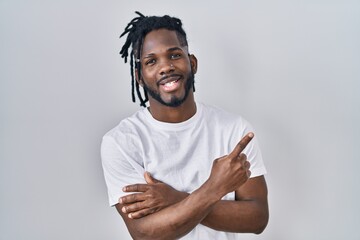 Wall Mural - African man with dreadlocks wearing casual t shirt over white background with a big smile on face, pointing with hand and finger to the side looking at the camera.