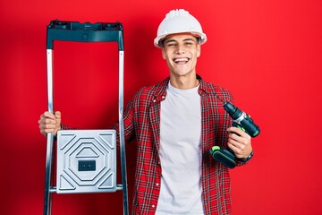 Wall Mural - Young hispanic man holding screwdriver wearing hardhat by construction stairs celebrating crazy and amazed for success with open eyes screaming excited.