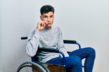 Canvas Print - Young hispanic man sitting on wheelchair mouth and lips shut as zip with fingers. secret and silent, taboo talking