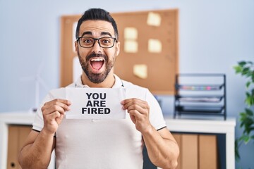 Sticker - Young hispanic man with beard holding you are fired banner at the office celebrating crazy and amazed for success with open eyes screaming excited.