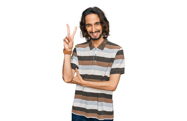 Poster - Young hispanic man wearing casual clothes smiling with happy face winking at the camera doing victory sign with fingers. number two.