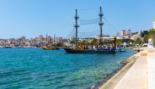 Scenic Cityscape Of Saranda On Coast Of Gulf Of Ionian Sea With Vintage Masted Wooden Sailing Ships For Sea Trips Moored Near Embankment On Sunny Day, Albania