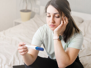 Wall Mural - the woman found out about an unwanted pregnancy. A woman with a pregnancy test in her hands is sitting on the bed in her apartment