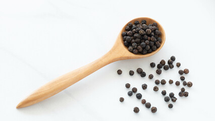 Wall Mural - Black peppercorn with a wooden spoon on white background. Composition isolated over the white background.