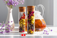 Tea With Flowers In A Glass Tea Jar. Glass Teapot With Brewed Drink. Advertising Tea Company, Concept, Presentation.
