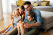 © NDABCREATIVITY - Happy young family having fun time at home. Parents with children using digital device.