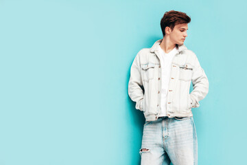 Portrait of handsome confident stylish hipster lambersexual model.Man dressed in jacket and jeans. Fashion male posing in studio near blue wall