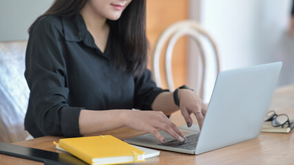 Wall Mural - Cropped shot female office worker using laptop computer on wooden office desk.