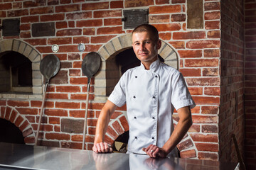 Portrait of a smiling pizza chef standing on the background of a wood-burning oven in the kitchen