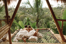 Happy Travel Couple On Hammock Balcony Of Bamboo Tree House With Jungle Nature View. Vacation In Beaitiful Hidden Place, Honeymoon On Bali Island