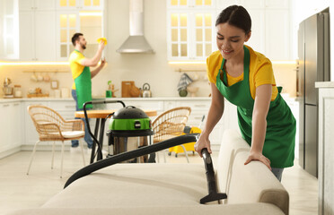 Poster - Professional janitor in uniform vacuuming sofa indoors