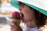 Mała dziewczynka w kapeluszu je lody truskawkowe, wakacyjna ochłoda, dzieci lubią lody