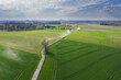 Równina pokryta łąkami i polami sfotografowana z drona.
Droga polna przebiegająca przez pola i łąki widziana z wysokości. Zdjęcie z drona. W oddali widać zabudowania pobliskiej wioski.