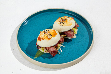 Bao buns with beef and vegetables. Chinese buns on ceramic plate on white background. Asian street food - bao with roast beef and fresh vegetables.