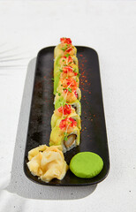 Canvas Print - Modern asian food - sushi roll with avocado and tuna on black plate on white concrete background.  Maki roll with avocado outside, tempura shrimp inside in minimal style. Fusion sushi menu.