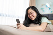 © Surachetsh - Beautiful glasses Asian woman lies on her stomach and plays mobile on the bed in her bedroom with a pastel green - brown color theme.