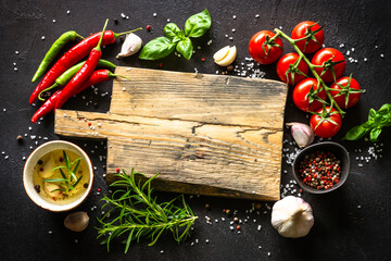 Food background. Oak cutting board, herbs, spices and fresh vegetables at dark kitchen table. Top view with space for design.