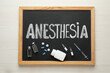 © New Africa - Blackboard with word Anesthesia, syringe and drugs on white wooden table, top view